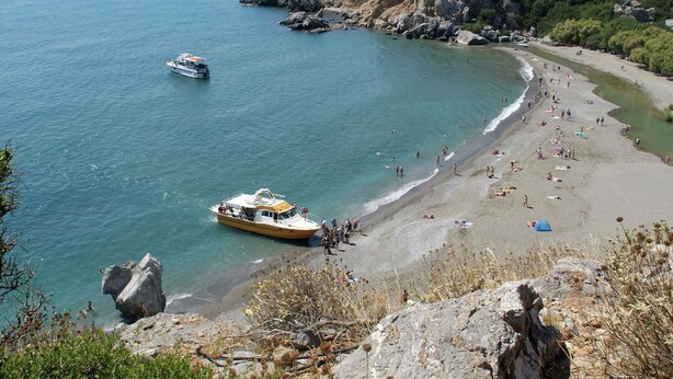 Una playa costera con terreno rocoso y un barco amarrado cerca de la orilla.