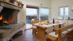 A cozy kitchen with a stone fireplace, wooden furniture, and a view of the mountains through the open door. - Detached Villa With Private Pool Located on Hill Overlooking Kvarner (Labin)