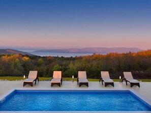 Una piscina con cuatro sillas reclinables y vistas a un lago y montañas.