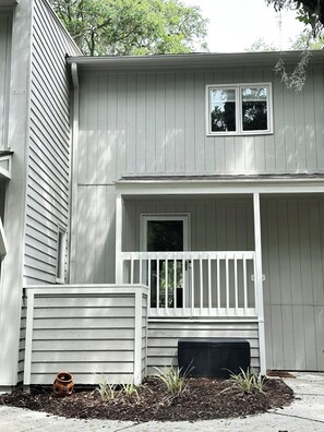 A two-story house with a front porch, a small garden area with plants, and a window.