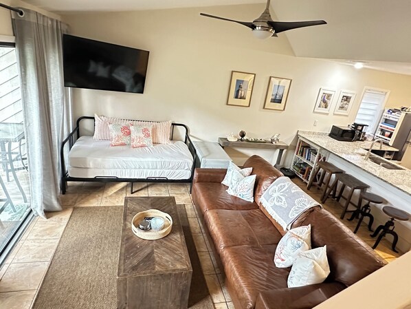 A modern living room with a bed, a brown leather sofa, a coffee table, and a kitchen area with a bar.