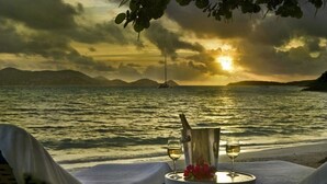 Ein Tisch am Strand mit einer Flasche und Gläsern, vor einer Sonnenuntergangsszene.
