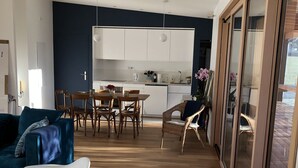 Uma sala de estar moderna com um sofá azul, uma cadeira de balanço branca e uma área de jantar com cadeiras de madeira.