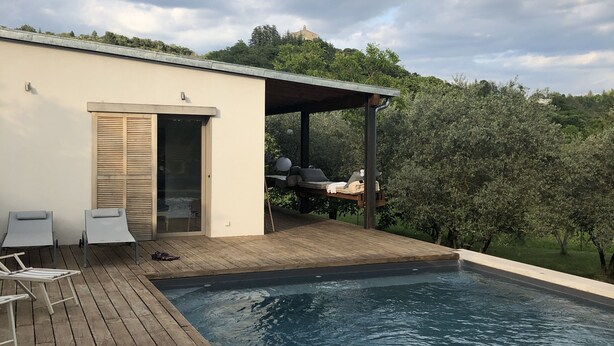 Piscina com deck de madeira, espreguiçadeiras e área de estar coberta.