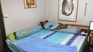 Un dormitorio con cama, almohadas, una manta azul, un escritorio con computadora y una pared decorada con cuadros.
