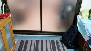 Una habitación con un alfombra a rayas, una cama con cubrecama estampado, un armario de madera y una puerta con panel de vidrio esmerilado.