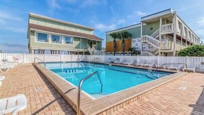 A swimming pool with lounge chairs, a building with a balcony, and a clear sky. - Entire Pensacola Beach Condo at Boardwalk (Pensacola Beach)