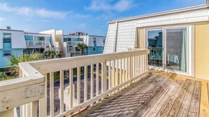 A wooden deck with a white railing, a glass door, and a view of neighboring buildings. - Entire Pensacola Beach Condo at Boardwalk (Pensacola Beach)