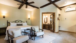 Une chambre à coucher avec un grand lit, deux fauteuils, une petite table et un ventilateur de plafond.