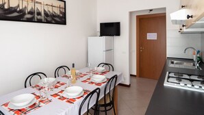 A dining area with a table set for four, a refrigerator, a television mounted above it, and a kitchen area with a stove. - Casa Paola 2 - Near the city center (Mestre)