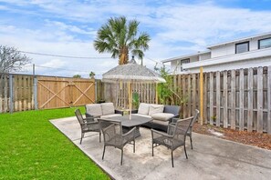 A patio with a round table and chairs, a covered seating area, and a wooden fence.