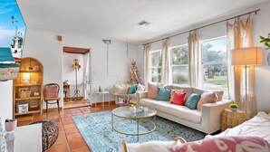 A spacious living room with a large window, a sofa, a coffee table, and a hanging chair. - Walk to Downtown St. Augustine, Boho Chic Bungalow (St. Augustine)