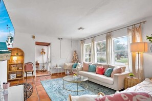 A spacious living room with a large window, a sofa, a coffee table, and a hanging chair.