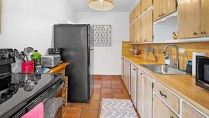 Une cuisine de taille réduite avec un réfrigérateur noir, des armoires en bois, un pare-feu en carrelage et un luminaire suspendu.