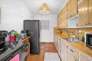 A compact kitchen with a black refrigerator, wooden cabinets, a tiled backsplash, and a hanging light fixture. - Walk to Downtown St. Augustine, Boho Chic Bungalow (St. Augustine)