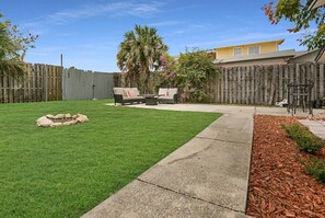 Ein Garten mit Rasen, einem Betonweg, einem Holzzaun und einer Terrasse mit Gartenmöbeln.
