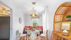 A dining area with a round table, white chairs, and a wicker chair. There is a sofa with orange cushions in the background. - Walk to Downtown St. Augustine, Boho Chic Bungalow (St. Augustine)