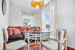 A room with a glass dining table surrounded by wicker chairs, a sofa with red cushions, and a hanging light fixture. - Walk to Downtown St. Augustine, Boho Chic Bungalow (St. Augustine)