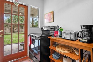 Une cuisine compacte avec un fourneau noir, un grille-pain et une machine à café, le tout posé sur une étagère en bois.