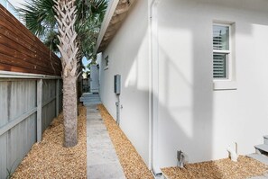A narrow pathway flanked by a wooden fence and a white building with a window and a small staircase. - 100 Steps to Beach, Deck w Ocean View, Beach Gear (St. Augustine)