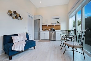 A modern kitchen with white cabinets, stainless steel appliances, and a dining area with metal chairs. - 100 Steps to Beach, Deck w Ocean View, Beach Gear (St. Augustine)