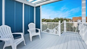 A covered outdoor area with two white Adirondack chairs, a white railing, and a view of the sky and distant buildings. - 100 Steps to Beach, Deck w Ocean View, Beach Gear (St. Augustine)