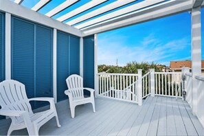 A covered outdoor area with two white Adirondack chairs, a white railing, and a view of the sky and distant buildings. - 100 Steps to Beach, Deck w Ocean View, Beach Gear (St. Augustine)