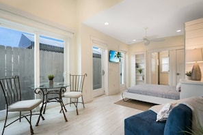A modern living room with a glass dining table, two chairs, a sofa, a TV, and a ceiling fan. - 100 Steps to Beach, Deck w Ocean View, Beach Gear (St. Augustine)