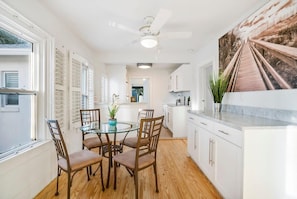 A modern kitchen with white cabinets, a glass dining table, and a ceiling fan. - 100 Steps to Sand, Private Deck, BBQ, Beach Gear (St. Augustine)
