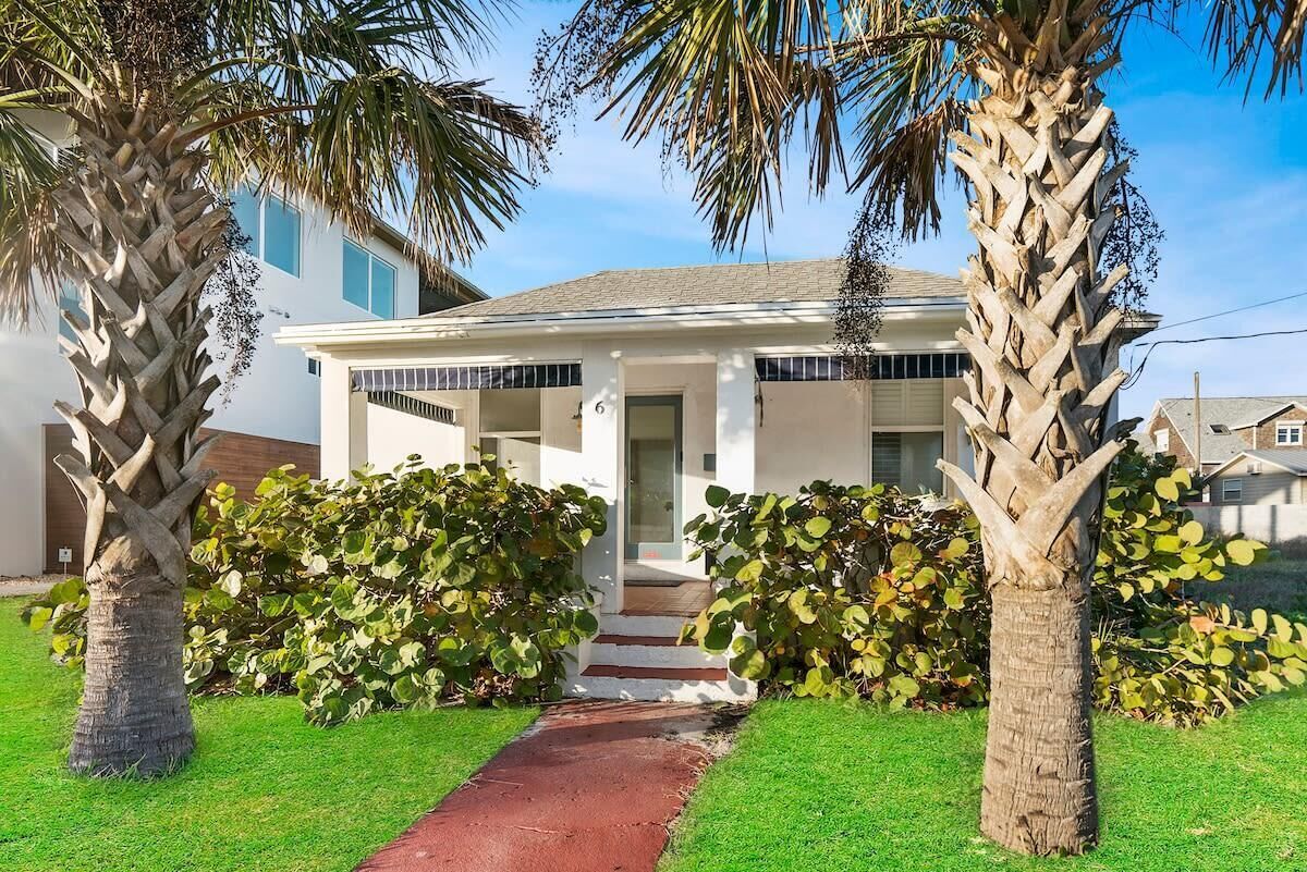 A modern two-story house with a front porch, a red pathway leading to the entrance, and two palm trees.