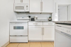 A kitchen with white cabinets, a microwave, a stove, and a coffee maker.