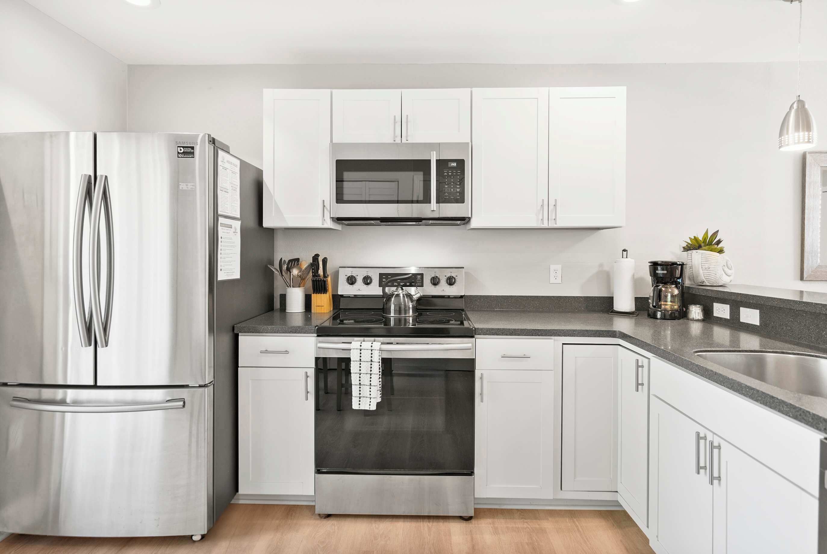 A modern kitchen with stainless steel appliances, white cabinetry, and a granite countertop.