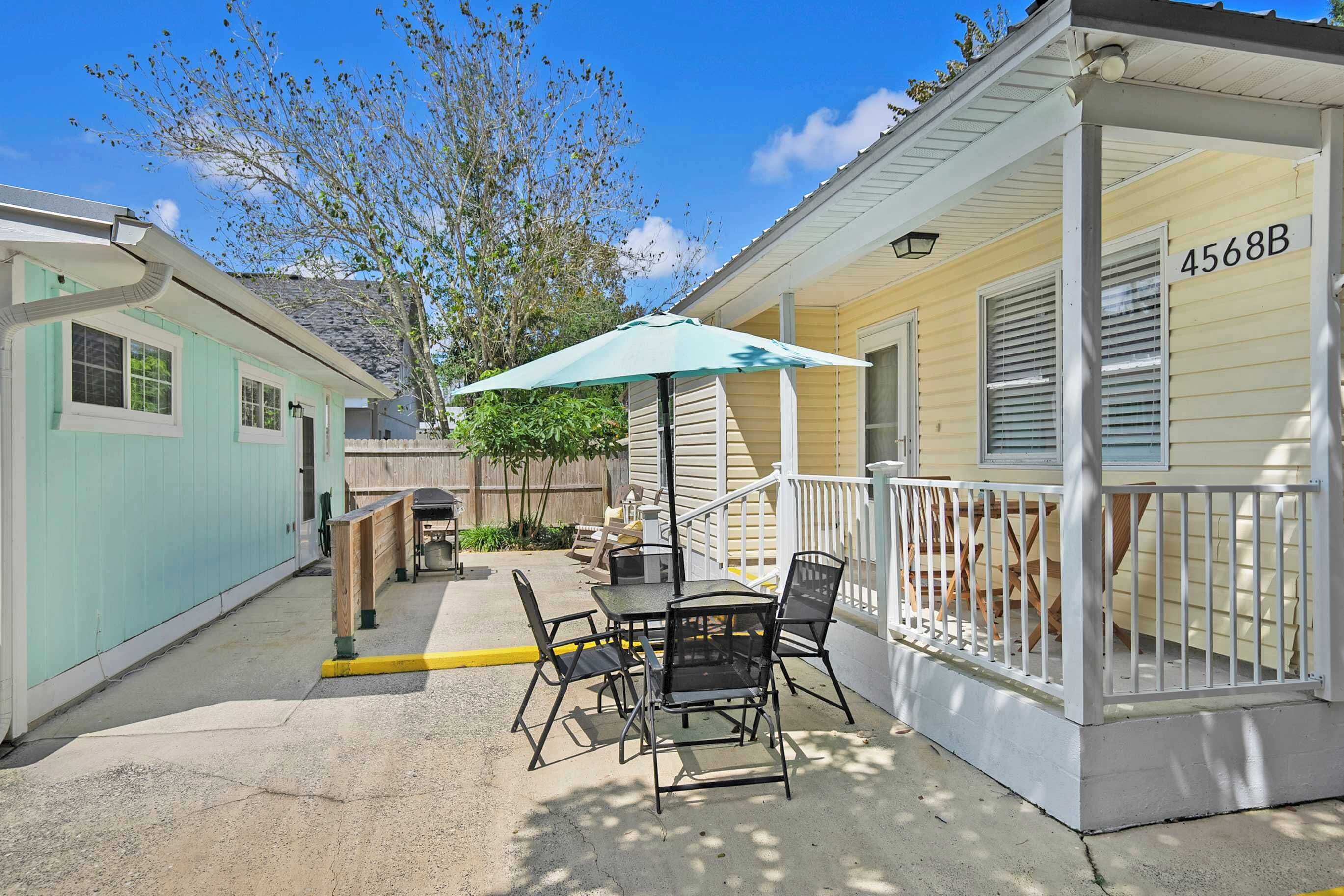 A covered outdoor patio with a table and chairs, a green umbrella, and a wooden fence.