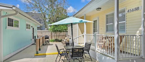 A covered outdoor patio with a table and chairs, a green umbrella, and a wooden fence.