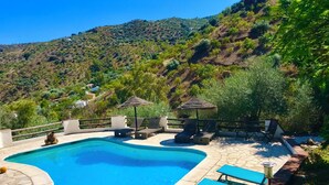 A swimming pool with lounge chairs and umbrellas, surrounded by a stone deck and lush greenery. - Large traditional CORTIJO, Large Private pool, Ping Pong table , family/groups (Malaga)