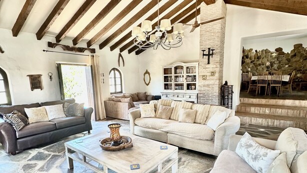 A spacious living room with a stone floor, wooden beams, a chandelier, and a stone wall with a fireplace. - Large traditional CORTIJO, Large Private pool, Ping Pong table , family/groups (Malaga)