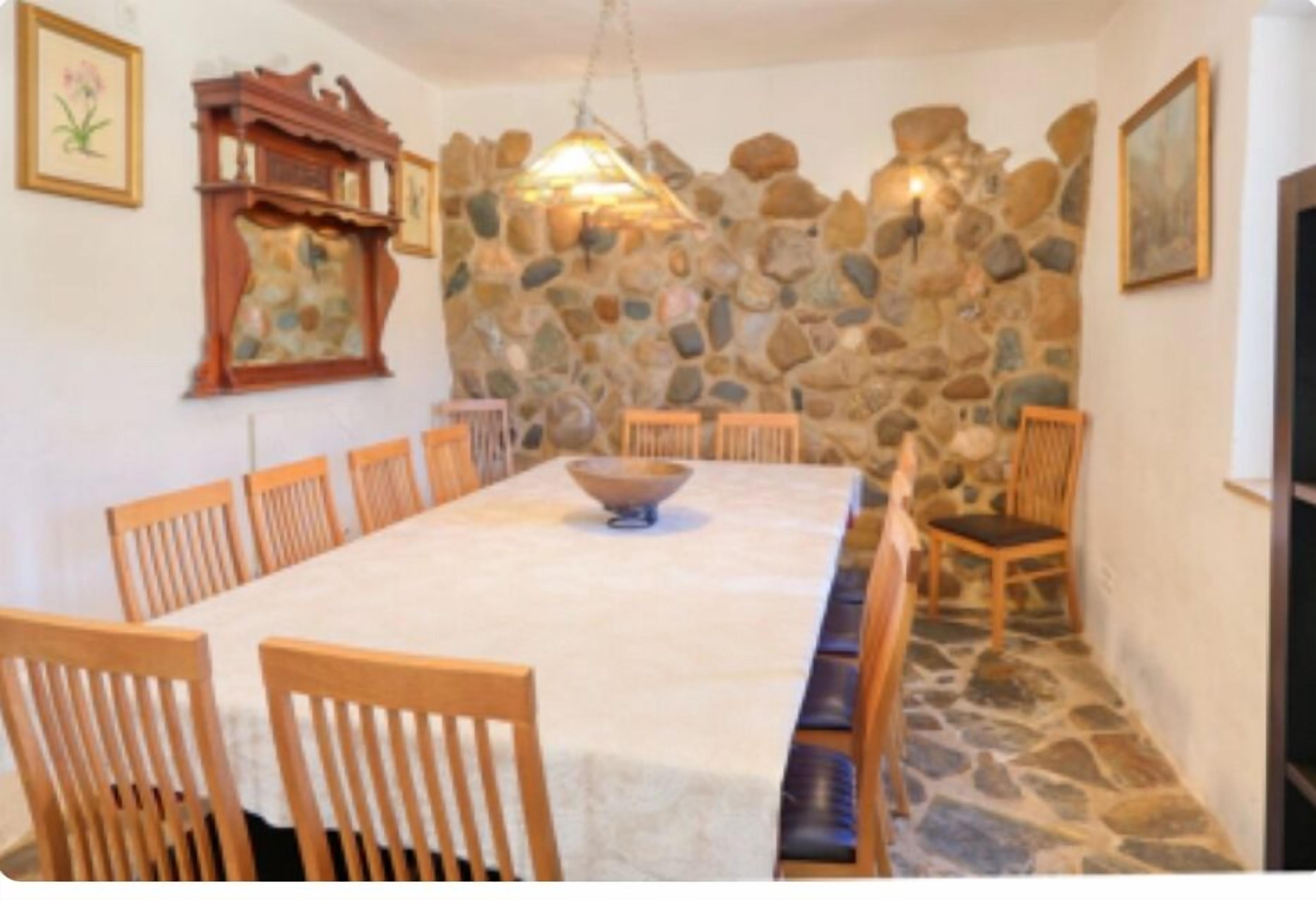 Ein Essbereich mit Steinwand, Holzstühlen, einem langen Tisch und einer Pendelleuchte.