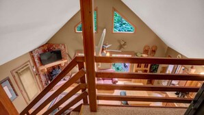 Quarto em estilo loft com teto inclinado, vigas de madeira e vista para o verde lá fora.