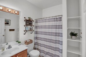 A bathroom with a white sink, a toilet, a striped shower curtain, a "WASH YOUR HANDS clean 100%" sign, and a small plant on the wall. - The Hideaway -Raystown Lake Vacation Rentals, Aunt Susie's (Hesston)