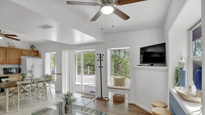 A spacious living area with a glass coffee table, wooden chairs, a TV mounted on the wall, and a ceiling fan. - The Hideaway -Raystown Lake Vacation Rentals, Aunt Susie's (Hesston)