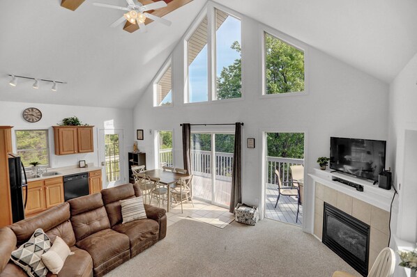 A spacious living area with a high ceiling, a fireplace, a television, and a dining area with a view of the outdoors. - The Hideaway -Raystown Lake Vacation Rentals, Aunt Susie's (Hesston)