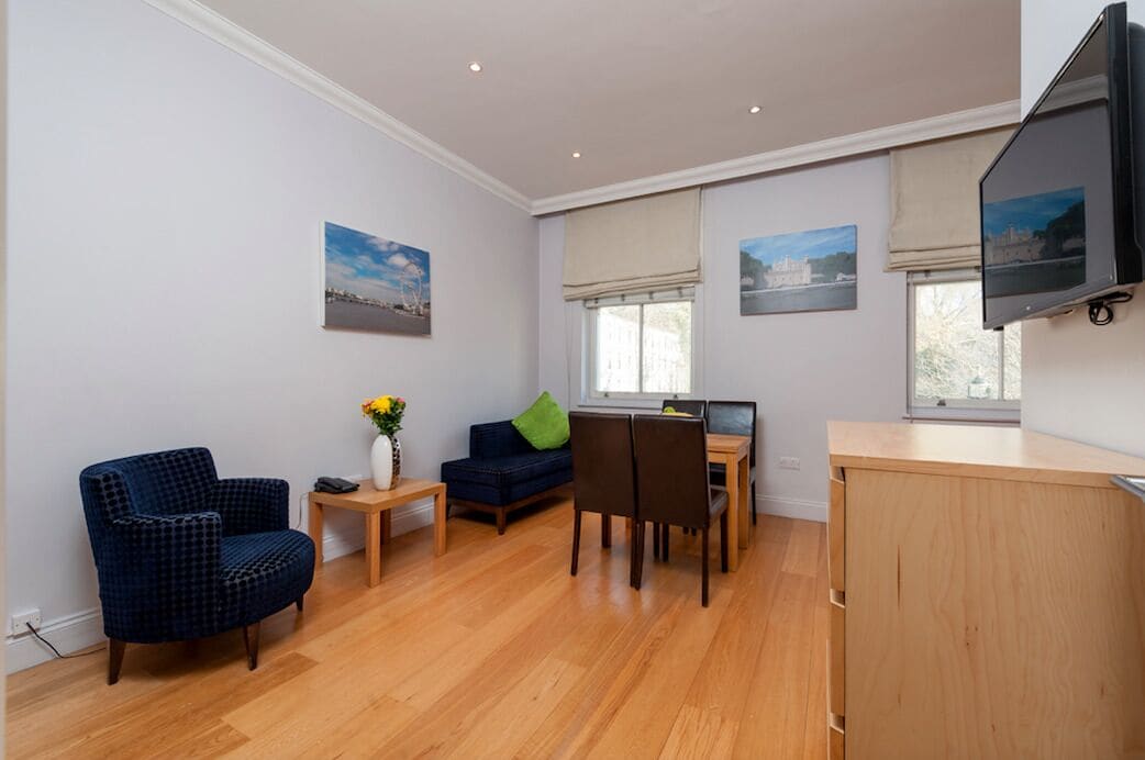 Ein modernes Wohnzimmer mit blauem Sessel, einer Couch, einem Esstisch mit Stühlen und einem an der Wand befestigten Fernseher.