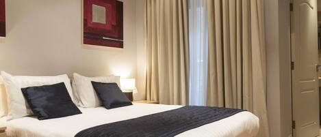 A hotel room with a large bed, two bedside tables, a lamp, and a window with curtains.