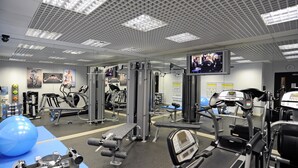 A gym with various exercise equipment, a large screen, and a blue exercise ball. - 12 London Street Apartments (London)