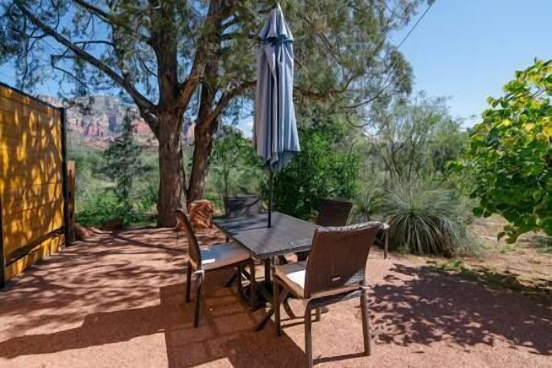 An outdoor dining area with a table and chairs, surrounded by trees and plants.