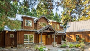 Ein zweistöckiges Holzhaus mit Steinfundament, einer Veranda und einem gepflegten Garten mit Steinen und Pflanzen.