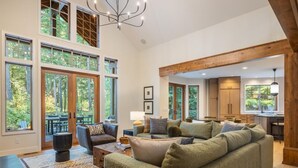 Ein geräumiges Wohnzimmer mit einem großen, grünen Sofa, einem Couchtisch und einem Teppich. Mehrere Fenster bieten einen Blick ins Freie.