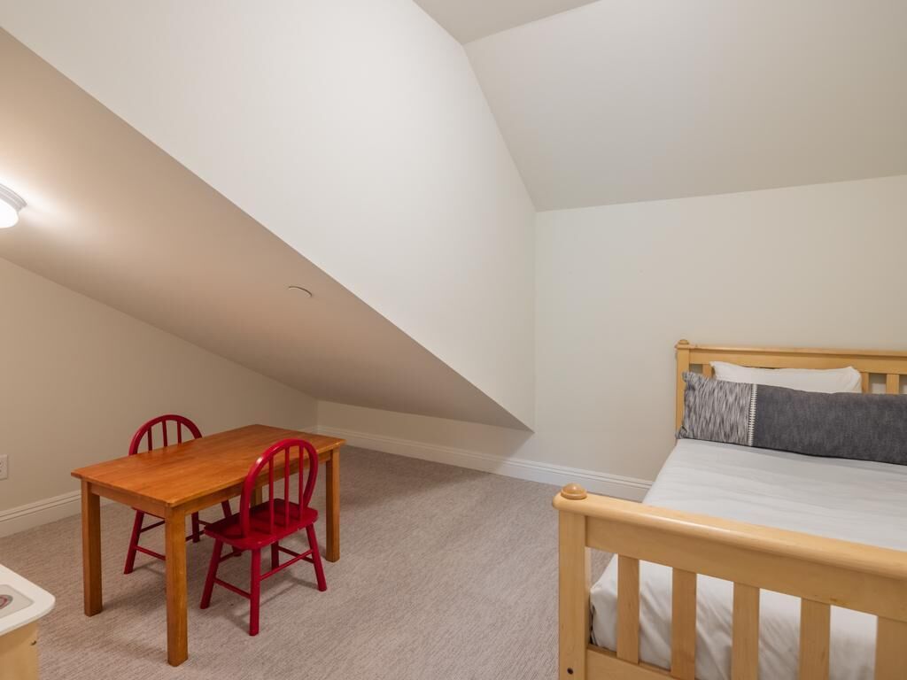 A bedroom with a wooden bed, a small table with two red chairs, and a carpeted floor.