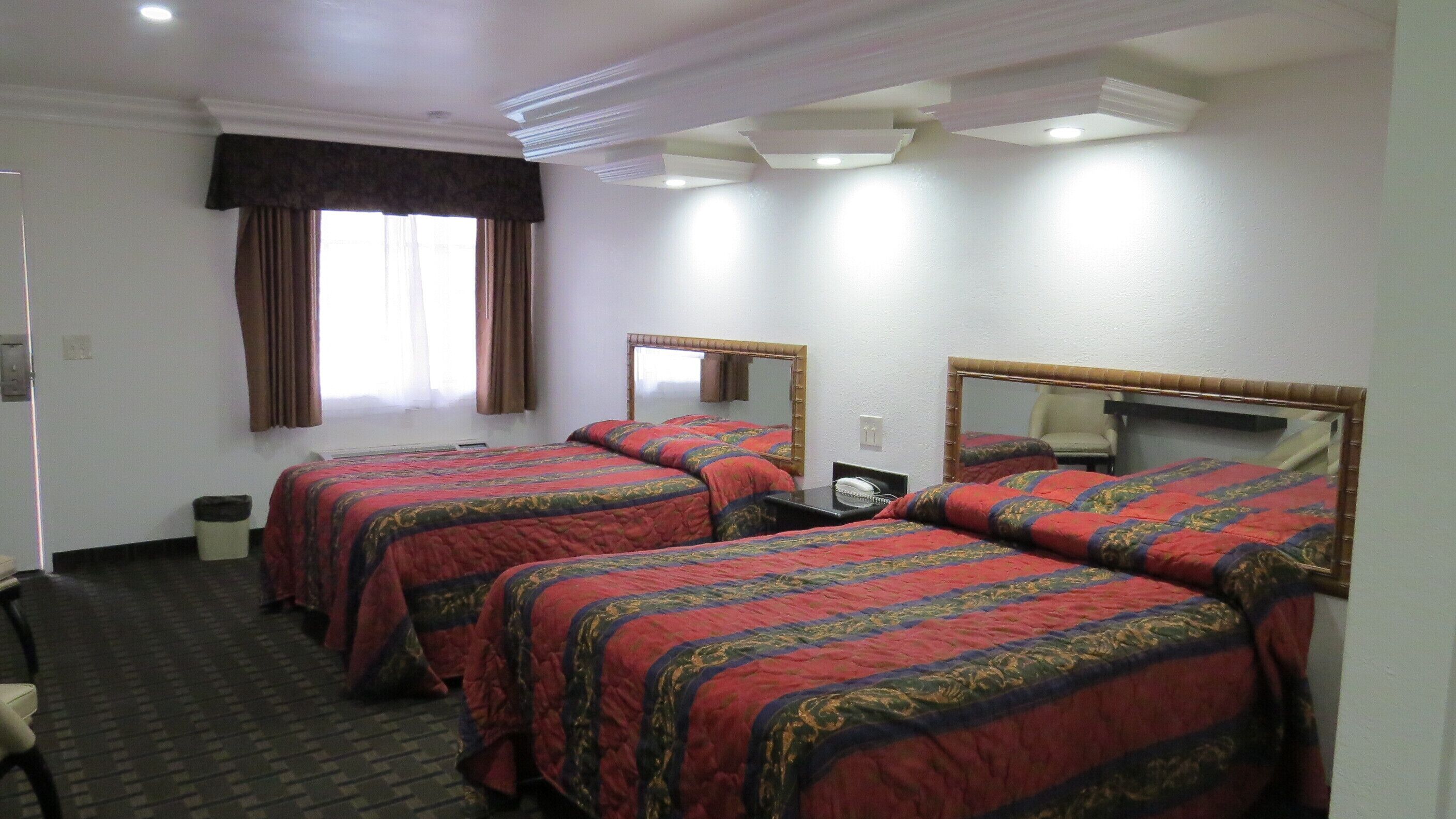 Habitación de hotel con dos camas, una silla, un escritorio con teléfono y una ventana con cortinas.