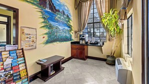 A hotel lobby with a mural of a mountain landscape, a coffee machine, a potted plant, and a promotional stand. - Rodeway Inn Santa Ana - Garden Grove (Santa Ana)